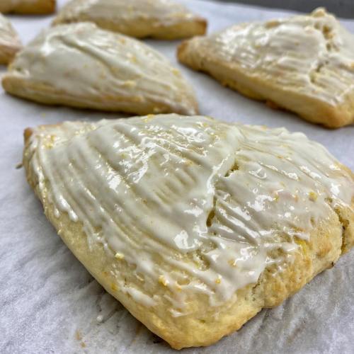 Freshly baked pastries with a glossy icing on a parchment-lined surface.