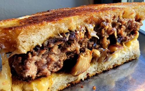 Close-up of a grilled sandwich filled with meat, melted cheese, and crispy edges on golden-brown bread.