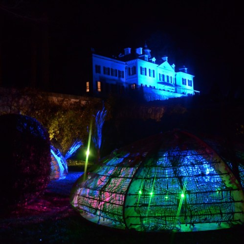 A brightly lit mansion at night, surrounded by colorful illuminated structures resembling tents in a garden.