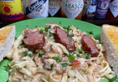A green plate with creamy pasta topped with sausage slices, garnished with green onions, and served with toasted bread.