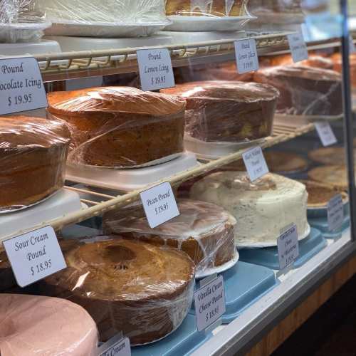 A display of various cakes, including pound cake and lemon loaf, each labeled with prices.