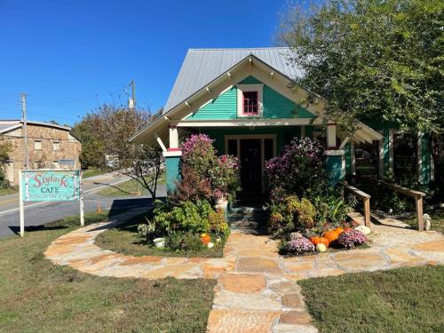 A charming café with a turquoise exterior, surrounded by colorful flowers and pumpkins, on a sunny day.