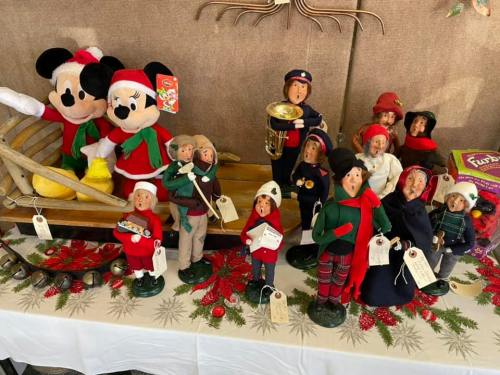 A festive display of dolls and figurines in holiday attire, alongside Mickey Mouse and a wooden sled.