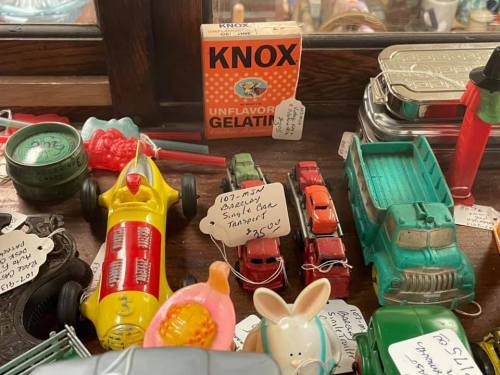 A collection of vintage toys and items, including a toy car, gelatin box, and various colorful trinkets on display.