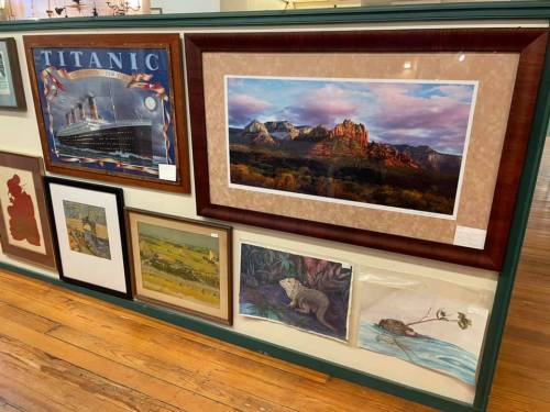 A gallery wall featuring various framed artworks, including a Titanic poster and landscape paintings.