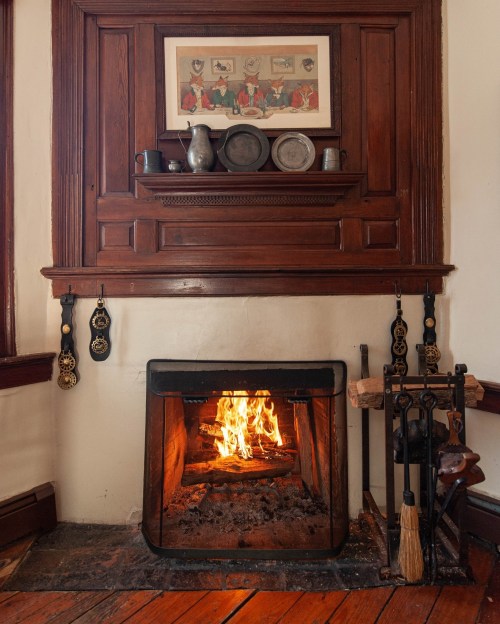 A cozy fireplace with a roaring fire, surrounded by wooden paneling and decorative items on the mantel.