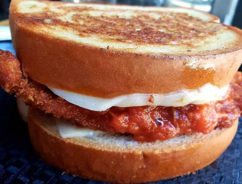 Close-up of a crispy chicken sandwich with melted cheese and sauce, served between two slices of toasted bread.