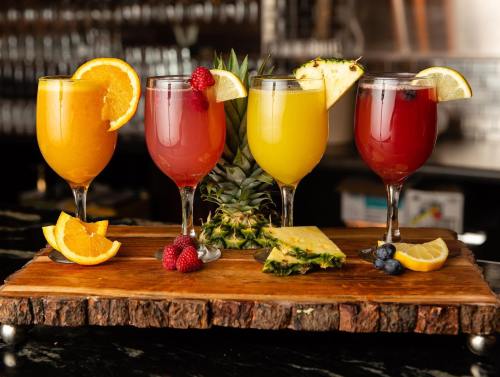 Four colorful cocktails on a wooden platter, garnished with fruit slices and surrounded by fresh pineapple.