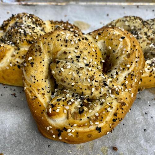 Freshly baked pretzels topped with a mix of sesame and poppy seeds, resting on a parchment-lined baking sheet.