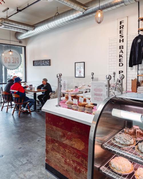 A cozy café interior with a display of baked goods, patrons seated, and a sign reading "Fresh Baked Pies."
