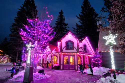 A cozy building adorned with vibrant pink lights, surrounded by snow and festive decorations, under a twilight sky.