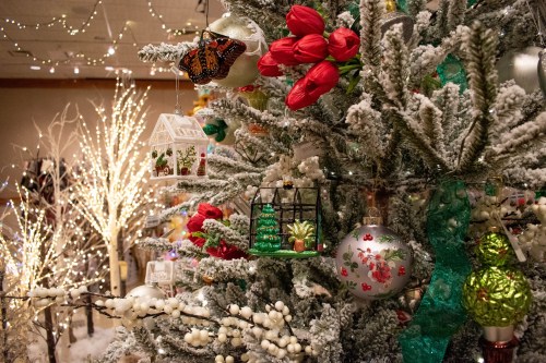 A decorated Christmas tree with red flowers, ornaments, and a butterfly, surrounded by twinkling lights and festive decor.