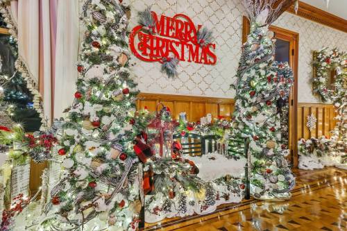 A festive Christmas display with decorated trees, garlands, and a "Merry Christmas" sign in a cozy indoor setting.