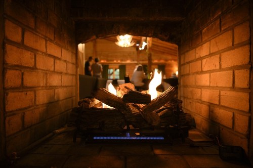 A cozy fireplace with burning logs, framed by brick, creating a warm atmosphere in a rustic setting.