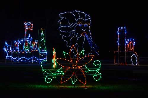 Colorful holiday lights display featuring a ship, castle, and a large flower in a nighttime setting.