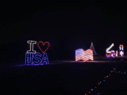 Colorful holiday lights display featuring "I ❤️ USA," an American flag, and festive decorations against a dark background.
