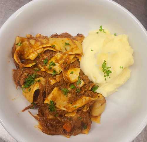 A bowl of pasta with rich meat sauce, garnished with parsley, alongside a serving of creamy mashed potatoes.