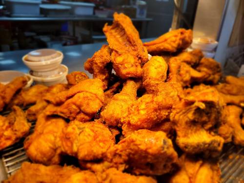 A close-up of a large pile of golden-brown fried chicken pieces, crispy and freshly cooked.
