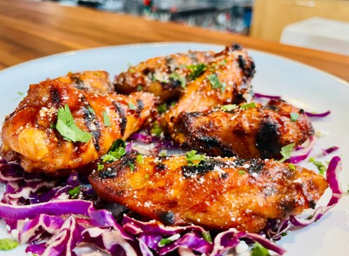 Grilled chicken wings garnished with herbs, served on a bed of purple cabbage.