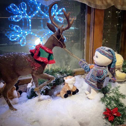 A child figure in winter attire pulls a reindeer with a festive collar, surrounded by snow and holiday decorations.