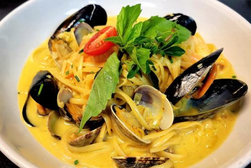 A bowl of pasta with mussels, clams, and herbs in a creamy yellow sauce, garnished with fresh basil and chili slices.