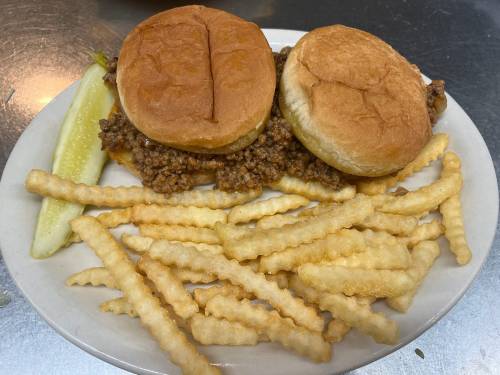 Two sandwich buns filled with seasoned meat, served with crinkle-cut fries and a pickle slice on a white plate.