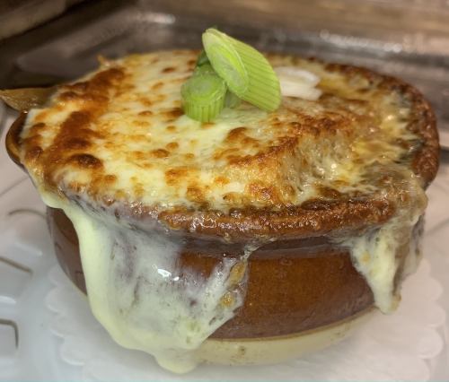 A bowl of French onion soup topped with melted cheese and green onions, with cheese bubbling over the sides.