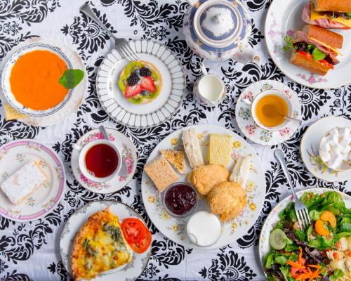 A beautifully arranged breakfast spread with tea, salads, pastries, and colorful fruits on a floral tablecloth.