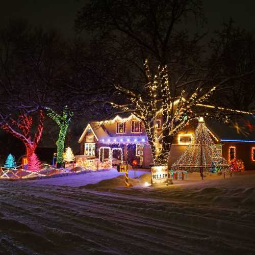 A snowy house decorated with colorful Christmas lights and a large tree, creating a festive winter scene.