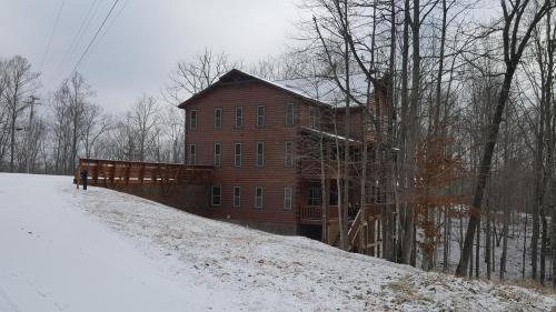 A large wooden house on a snowy hillside, surrounded by bare trees under a cloudy sky.