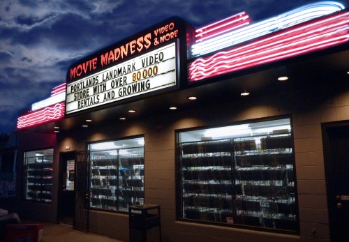 A video rental store with a neon sign reading "Movie Madness" and a marquee highlighting over 80,000 rentals.