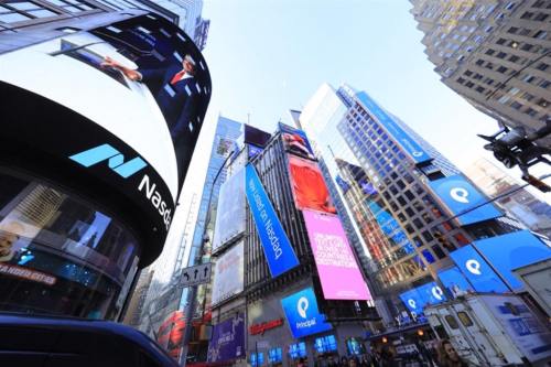 A bustling cityscape featuring large digital billboards in Times Square, New York City, under a clear blue sky.