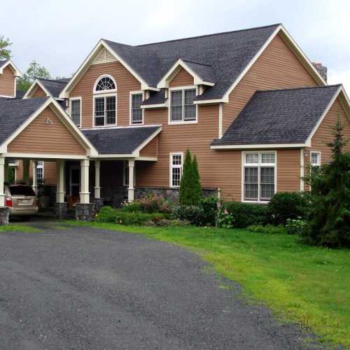 A large, two-story house with a brown exterior, multiple gables, and a landscaped front yard.