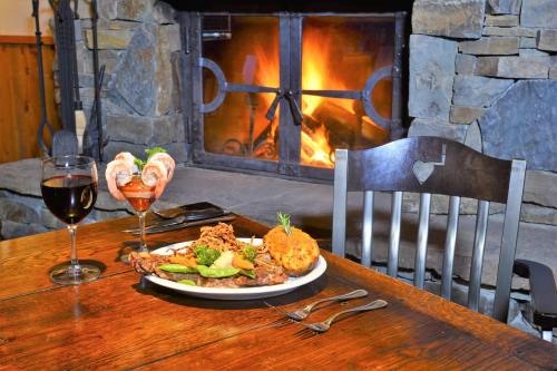 A cozy dining table with a plate of food, two drinks, and a warm fireplace in the background.