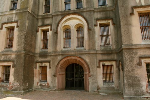 A weathered stone building with barred windows and a large arched entrance, showcasing an old, historic architectural style.
