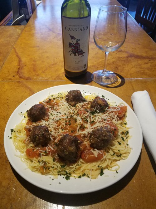 A plate of spaghetti topped with meatballs and cheese, accompanied by a bottle of Gabbiano Chianti and a wine glass.