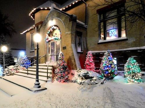 A festive building adorned with colorful lights and decorated trees, surrounded by snow at night.