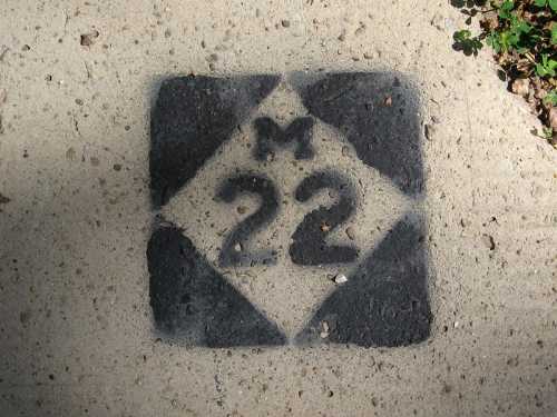 A square concrete marker with the letter "M" and the number "22" painted in black on a light-colored surface.