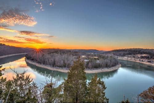 A scenic view of a river winding through a forested landscape at sunset, with vibrant colors in the sky.