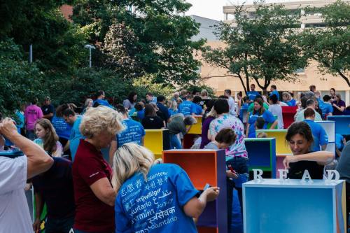 A diverse group of volunteers in blue shirts work together on colorful projects outdoors.