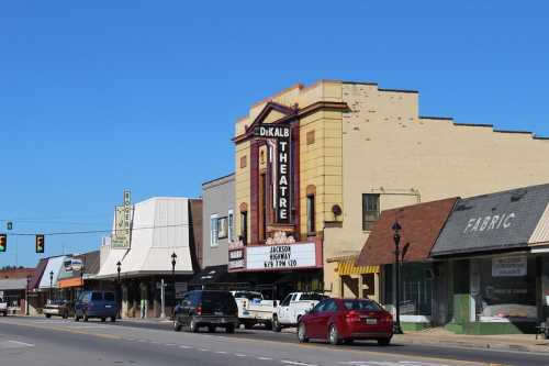 A street view of DeKalb Theatre with nearby shops and cars parked along the road under a clear blue sky.