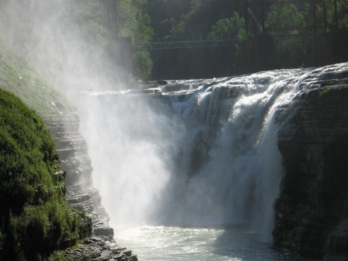 A waterfall cascading over rocky cliffs, surrounded by lush greenery and mist rising from the water.