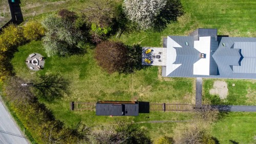 Aerial view of a green yard featuring a house, a patio, a fire pit, and a train car on tracks.