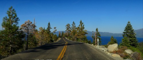 A scenic road lined with trees, leading towards a lake under a clear blue sky.