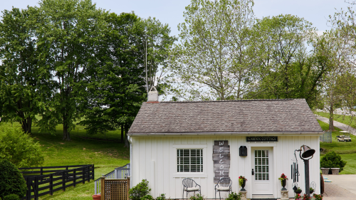 A charming white cottage with a sign reading "Garden Cottage," surrounded by greenery and trees.