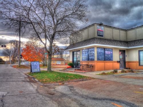 A small restaurant with a chalkboard sign, surrounded by autumn trees and a cloudy sky.