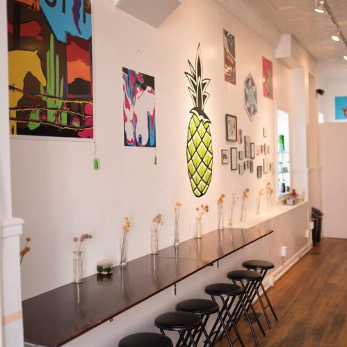 A bright, modern interior with colorful wall art, a wooden counter, and black stools along the wall.