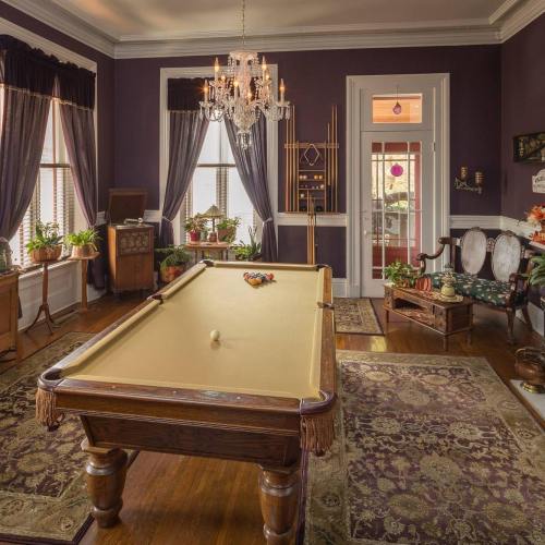 A cozy room with a pool table, elegant decor, plants, and a chandelier, featuring rich purple walls and vintage furniture.