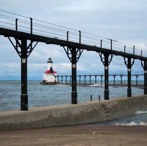 A lighthouse at the end of a pier, with calm waters and cloudy skies in the background.