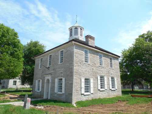 Historic stone building with a cupola, surrounded by green trees and a clear blue sky.